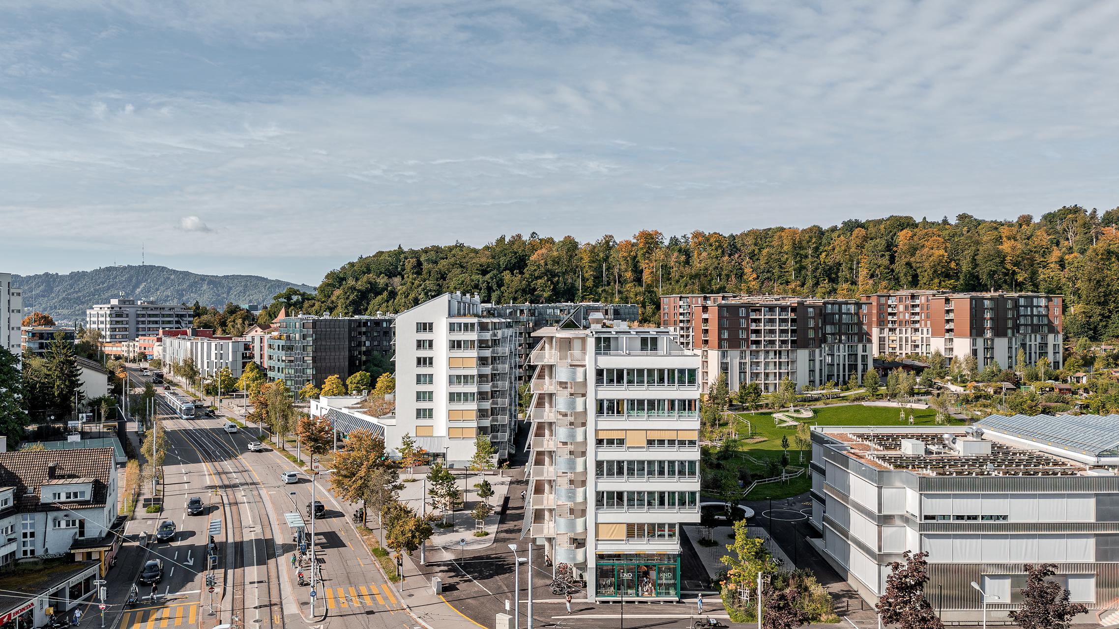 „Luftaufnahme von Zürich mit der Wohnüberbauung Guggach III im Vordergrund. Zu sehen sind moderne Wohngebäude und ein Schulkomplex mit Sport- und Spielplätzen. Im Hintergrund die Stadt mit Hochhäusern und grünen Baumreihen unter teils bewölktem Himmel. Entworfen von Donet Schäfer Reimer Architekten. Aufgenommen mit der DJI Mini 5 Pro.“