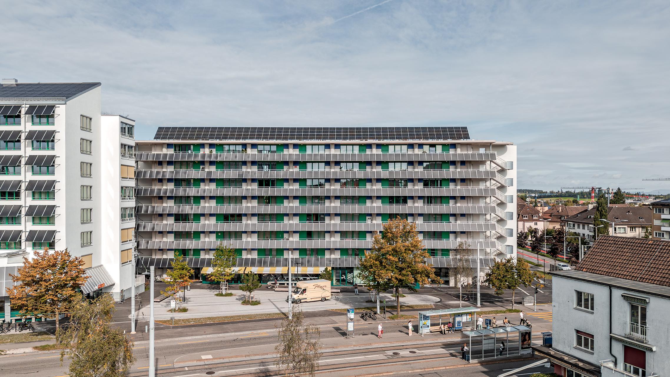 „Luftaufnahme von Zürich mit der Wohnüberbauung Guggach III im Vordergrund. Zu sehen sind moderne Wohngebäude und ein Schulkomplex mit Sport- und Spielplätzen. Im Hintergrund die Stadt mit Hochhäusern und grünen Baumreihen unter teils bewölktem Himmel. Entworfen von Donet Schäfer Reimer Architekten. Aufgenommen mit der DJI Mini 5 Pro.“