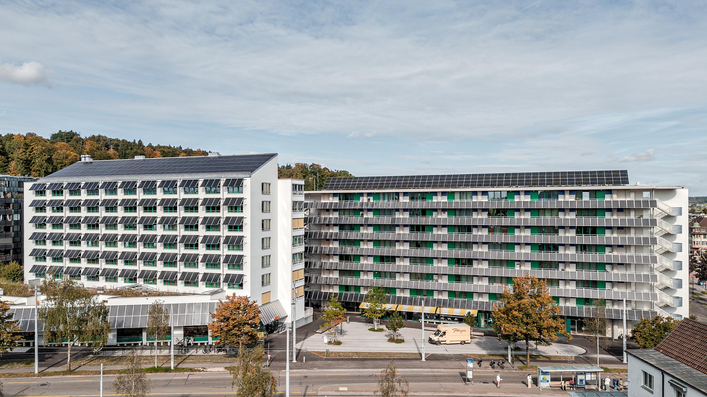 „Luftaufnahme von Zürich mit der Wohnüberbauung Guggach III im Vordergrund. Zu sehen sind moderne Wohngebäude und ein Schulkomplex mit Sport- und Spielplätzen. Im Hintergrund die Stadt mit Hochhäusern und grünen Baumreihen unter teils bewölktem Himmel. Entworfen von Donet Schäfer Reimer Architekten. Aufgenommen mit der DJI Mini 5 Pro.“